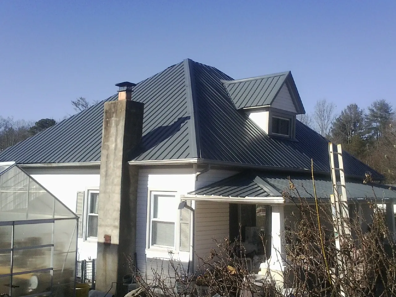 Dark blue standing seam metal roof on a white farmhouse with dormer — Slate & Tile Roof Repair by Roofing Brothers in Choctaw
