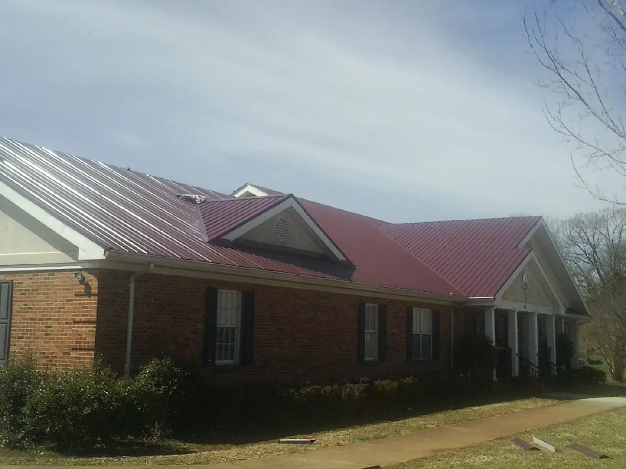Red metal roof with gabled entries on a long brick building, from a Hail Damage Roof Repair job in Choctaw