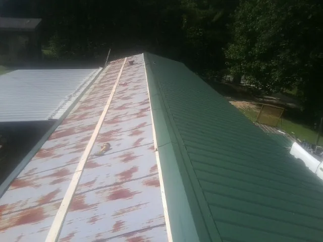 Old rusted panels beside newly installed green metal roofing — Wind Damage Roof Repair by Roofing Brothers in Choctaw