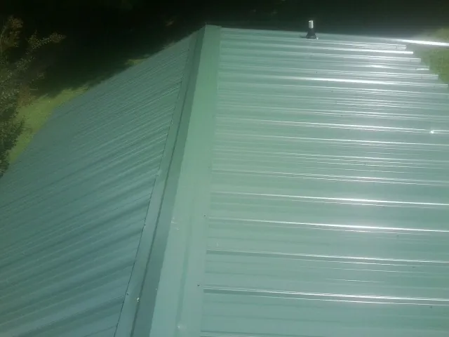 New green metal panels meeting at the ridge of a roof — Flat Roof Repair work by our crew in Choctaw