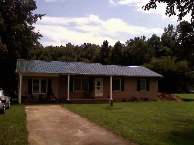 Dark green metal roof on a brick ranch with a covered porch in Choctaw