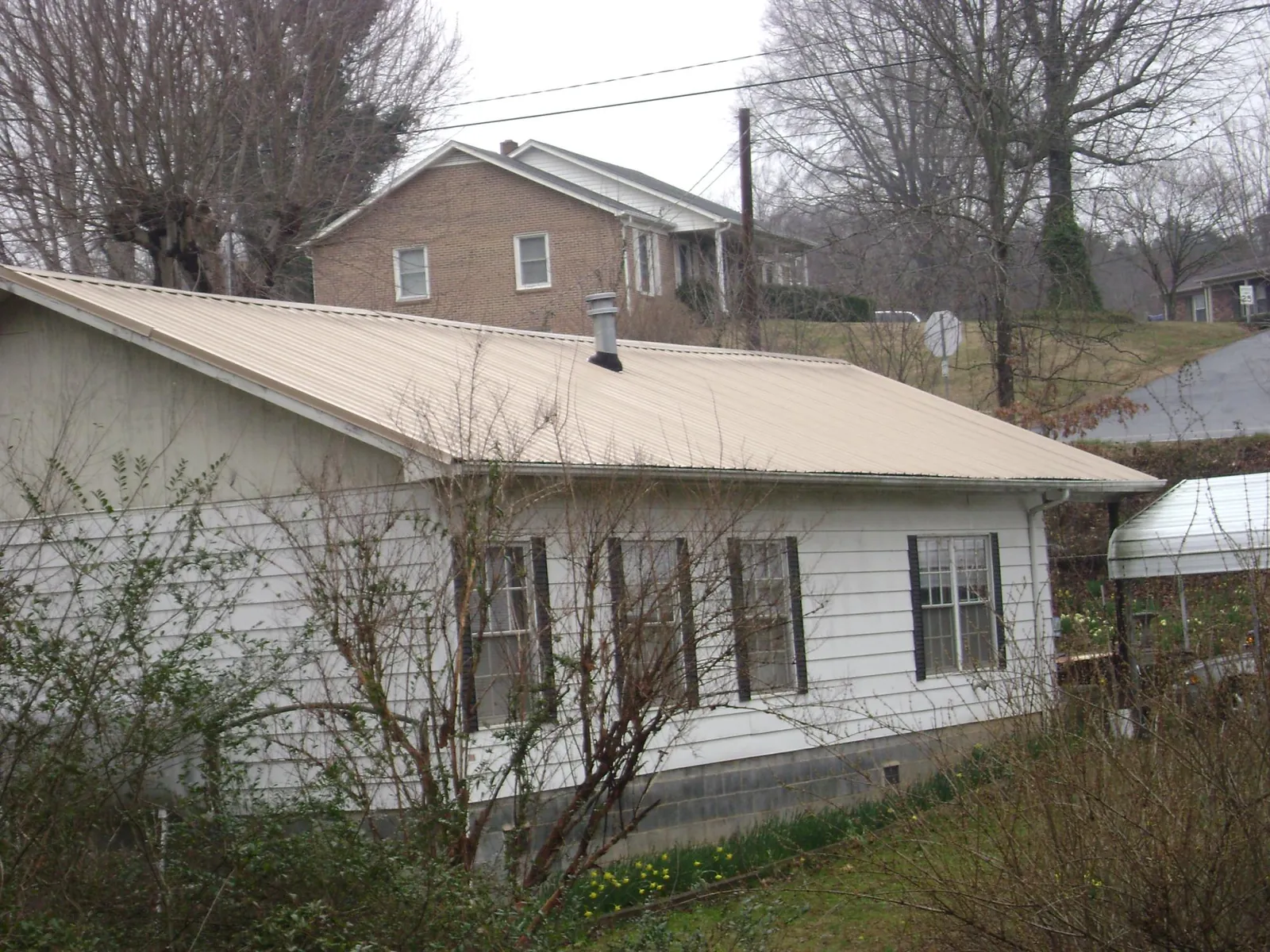 Tan metal roof on a white sided house set into a hillside — Commercial Roofing by Roofing Brothers in Choctaw