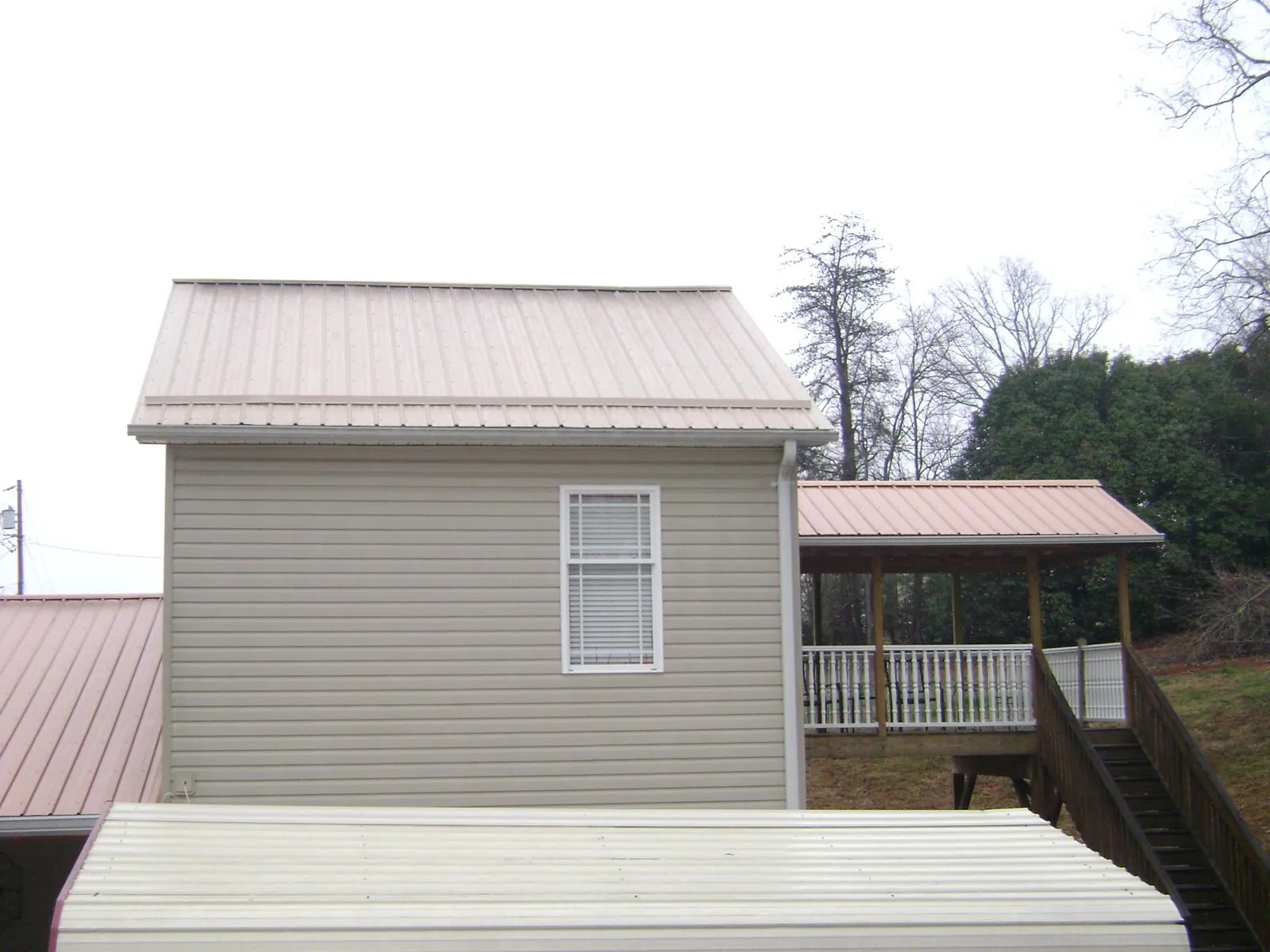 Tan metal roofs on a two story addition and attached porch, from a Roof Replacement job in Choctaw