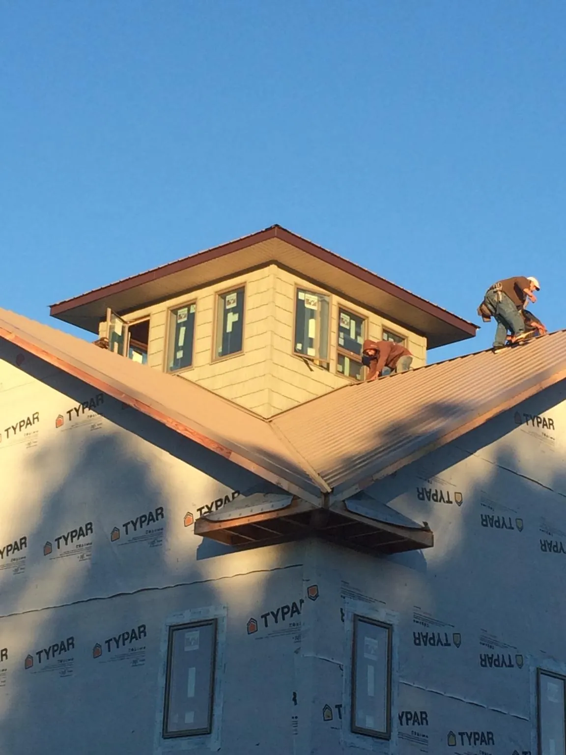 Roofers working around a rooftop cupola on a new metal roof at sunset — Roof Waterproofing in Choctaw by Roofing Brothers